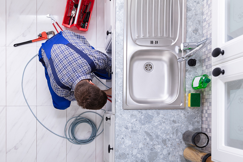 Young Male Plumber Cleaning Clogged Sink Pipe In Kitchen